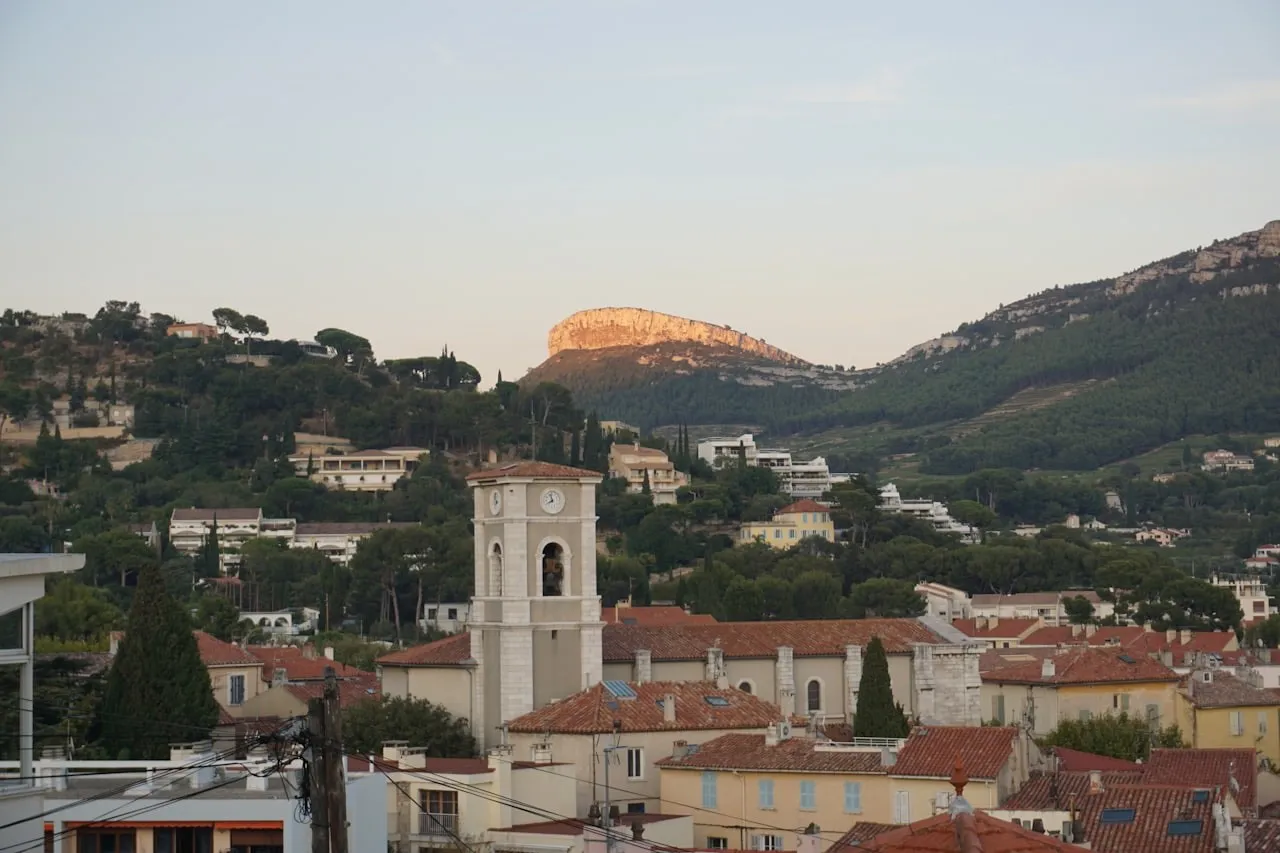 Village perché de l'arrière-pays méditerranéen au crépuscule : clocher et toits de tuiles sur un fond de collines boisées.